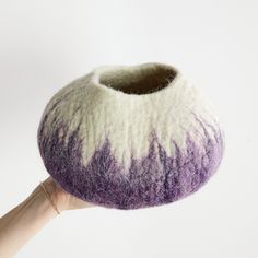 a hand is holding up a purple and white wool ball that has been made into a vase