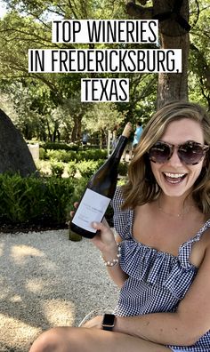 a woman sitting on the ground holding a bottle of wine in her hand and smiling