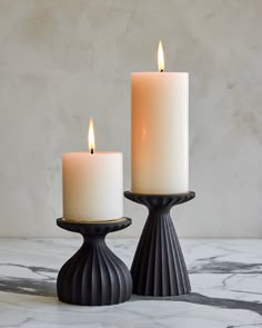 two white candles sitting next to each other on top of a marble countertopstone