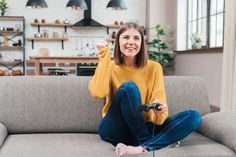 a woman sitting on a couch holding a remote control in one hand and smiling at the camera