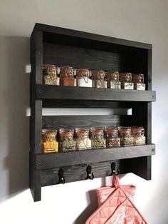 a shelf with jars and spices on it next to a wall mounted oven mitt