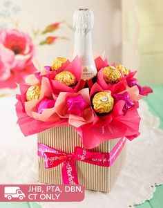 a bottle of champagne and chocolates in a gift box on a doily with pink flowers