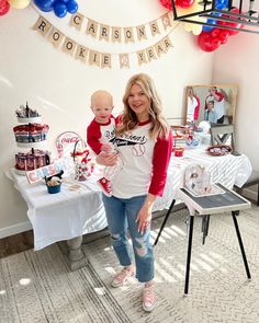 a woman standing next to a baby in front of a table with balloons and decorations