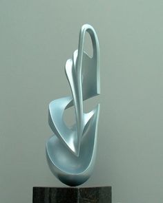 a silver sculpture sitting on top of a black marble block in front of a gray wall