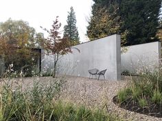 a chair sitting on top of a gravel field next to a cement wall and trees