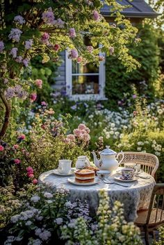 an outdoor table with tea and cake on it in the middle of a garden filled with flowers