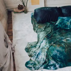 an unmade bed with blue and green comforter on the floor next to a plant