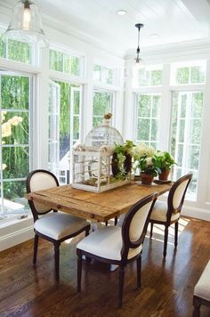 a birdcage sits on top of a wooden table surrounded by chairs and windows