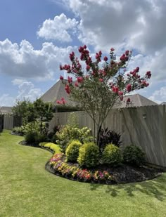 a garden with flowers and trees in the grass next to a fence on a sunny day