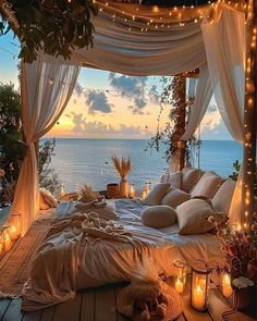 a bed covered in pillows and lights next to the ocean at night with candles lit up