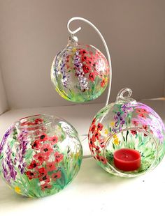 three glass vases with flowers painted on them and a red candle in the middle