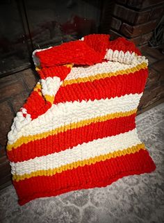 a red, white and yellow knitted blanket sitting on the floor