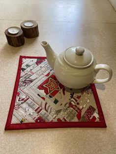 a tea pot sitting on top of a table next to two candles and a place mat