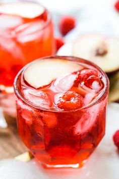 two glasses filled with raspberry punch on top of a wooden table next to sliced apples