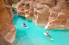 two people on jet skis in the middle of a river with cliffs and blue water