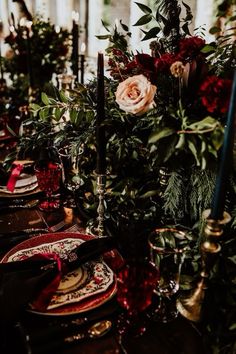 the table is set with red and gold plates, silverware, greenery and candles