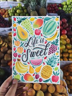 a person holding up a card that says life is sweet surrounded by lots of fruit