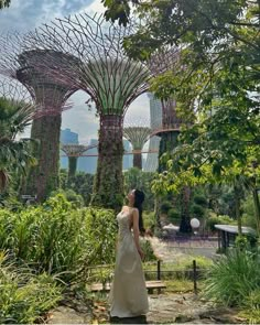 a woman in a white dress is looking at the trees and plants inside gardens by the bay