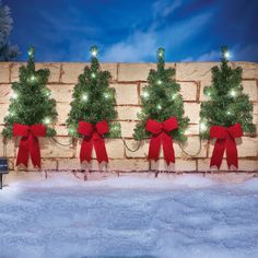 a brick wall decorated with christmas trees and red bows, surrounded by snow at night