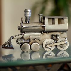 a metal toy train sitting on top of a glass table next to a potted plant