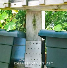 two blue bins with plants growing out of them on a wooden structure in the middle of a park