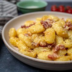 a white bowl filled with pasta covered in cheese and bacon sitting on top of a table