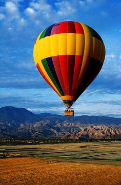 a colorful hot air balloon flying in the sky over a field with mountains behind it