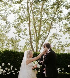 a bride and groom standing next to each other in front of a tree with white flowers