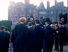 a group of young men in suits and top hats walking down a street with tall buildings behind them