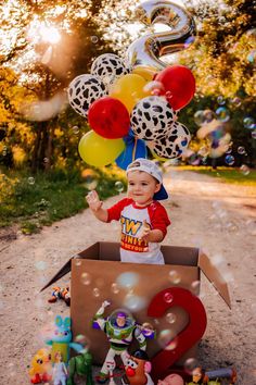 a little boy is sitting in a box with balloons and other toys on the ground