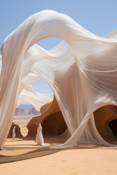 two people are standing in the desert with long white fabric draped over their heads and body