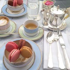 a table topped with plates and cups filled with desserts next to silver utensils