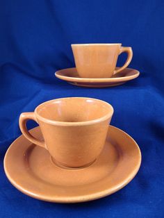 two brown cups and saucers sitting on top of each other with blue cloth behind them