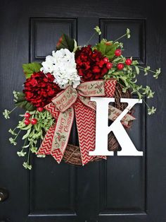 a wreath that has the letter k on it and flowers hanging from it's front door