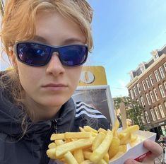 a woman in sunglasses is eating french fries