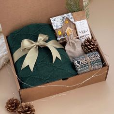 a christmas gift box filled with gifts and wrapped in green fabric, pine cones, and twine