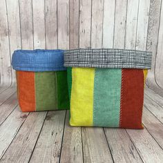 two colorful striped bags sitting on top of a wooden floor with wood boards behind them