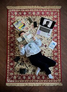 a woman laying on top of a red rug next to a laptop and other items