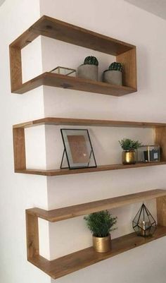 three wooden shelves on the wall with plants and pictures in them, one is empty