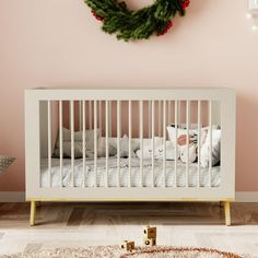 a white crib in front of a pink wall with a wreath on the wall