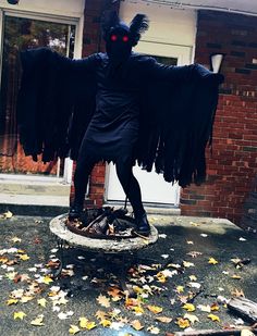 a person in a black costume with wings on top of a white table and leaves scattered all over the ground