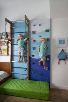 two young children climbing up and down the wall in a bedroom with green bedding