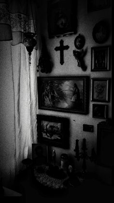 black and white photograph of the corner of a room with pictures on the wall, candles in vases and paintings