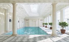 an indoor swimming pool with columns and potted plants