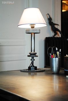 a lamp sitting on top of a wooden table next to a cup and pen holder