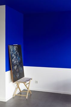 an easel in front of a blue and white wall with a painting on it