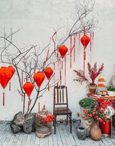 red lanterns hanging from the side of a white wall next to a chair and potted plants