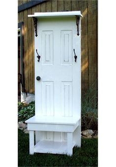 a white bench sitting in front of a wooden door with hooks on it's sides