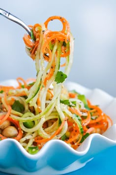 a fork is lifting up some veggie salad from a white bowl on a blue tablecloth