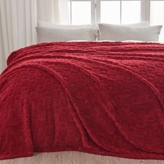 a red bedspread with white pillows in front of a window and wooden floor